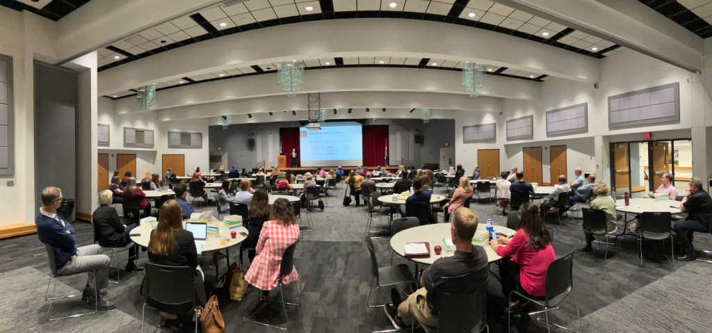 Flower Darby presenting to an audience of faculty and staff, who are sitting at tables filling a university ballroom.